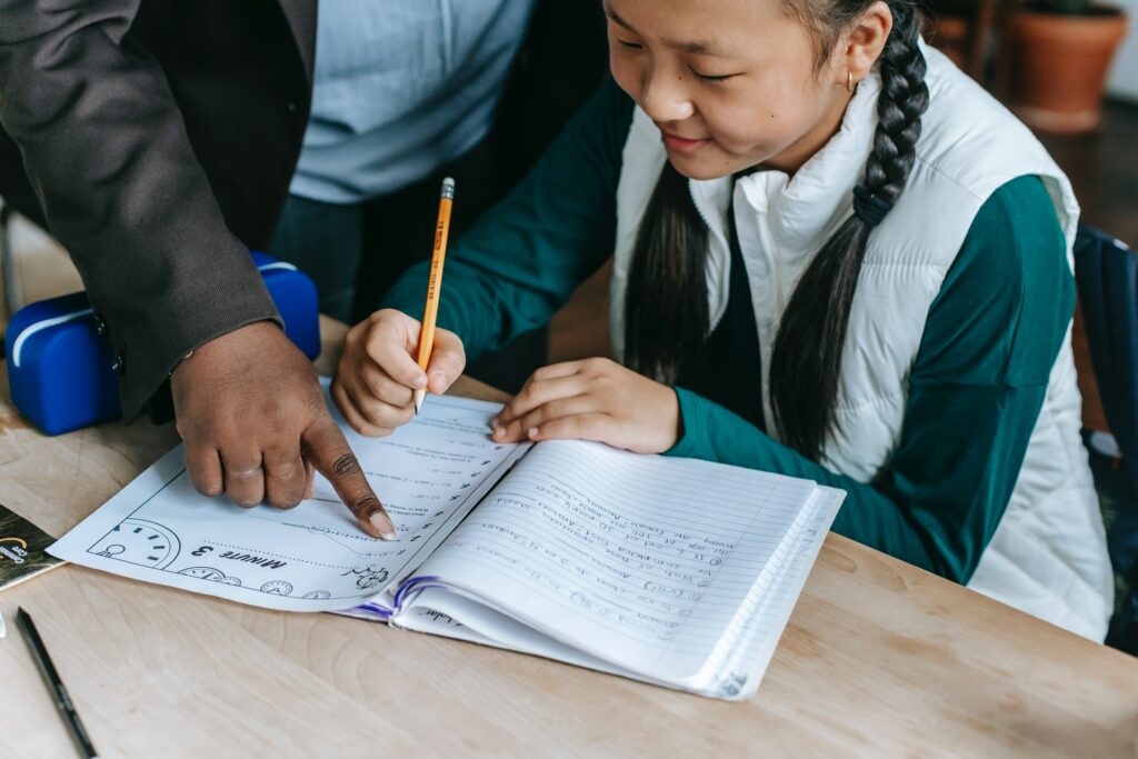 child at school working at a desk in their exercise books getting help from their teacher
