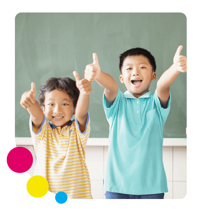Two students in bright clothing standing in front of a chalk board with their thumbs up
